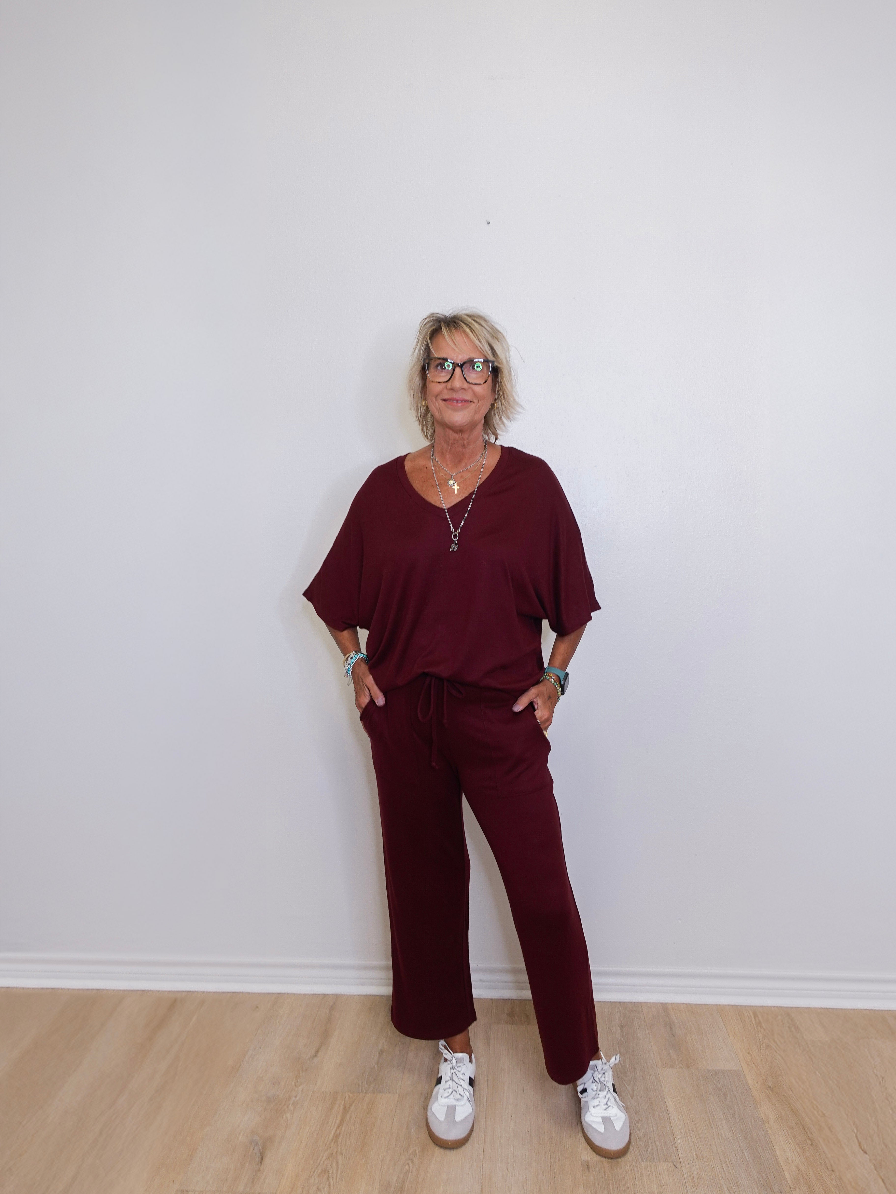 Woman wearing a burgundy outfit with white sneakers against a plain white wall.