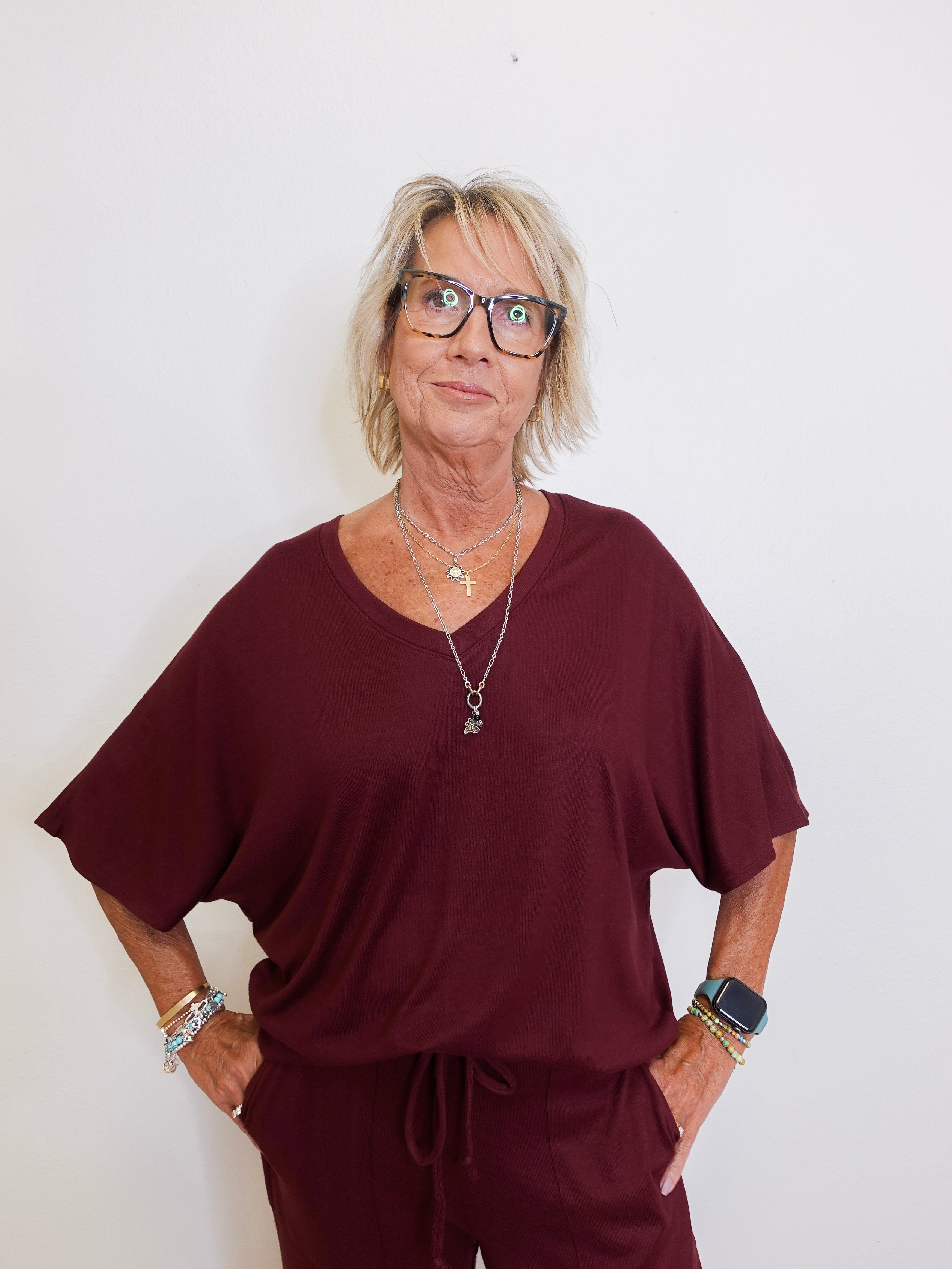 Woman wearing a burgundy outfit with glasses against a white background