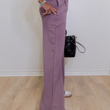 Person wearing a matching purple outfit with wide-leg pants and a black bag on a wooden floor.