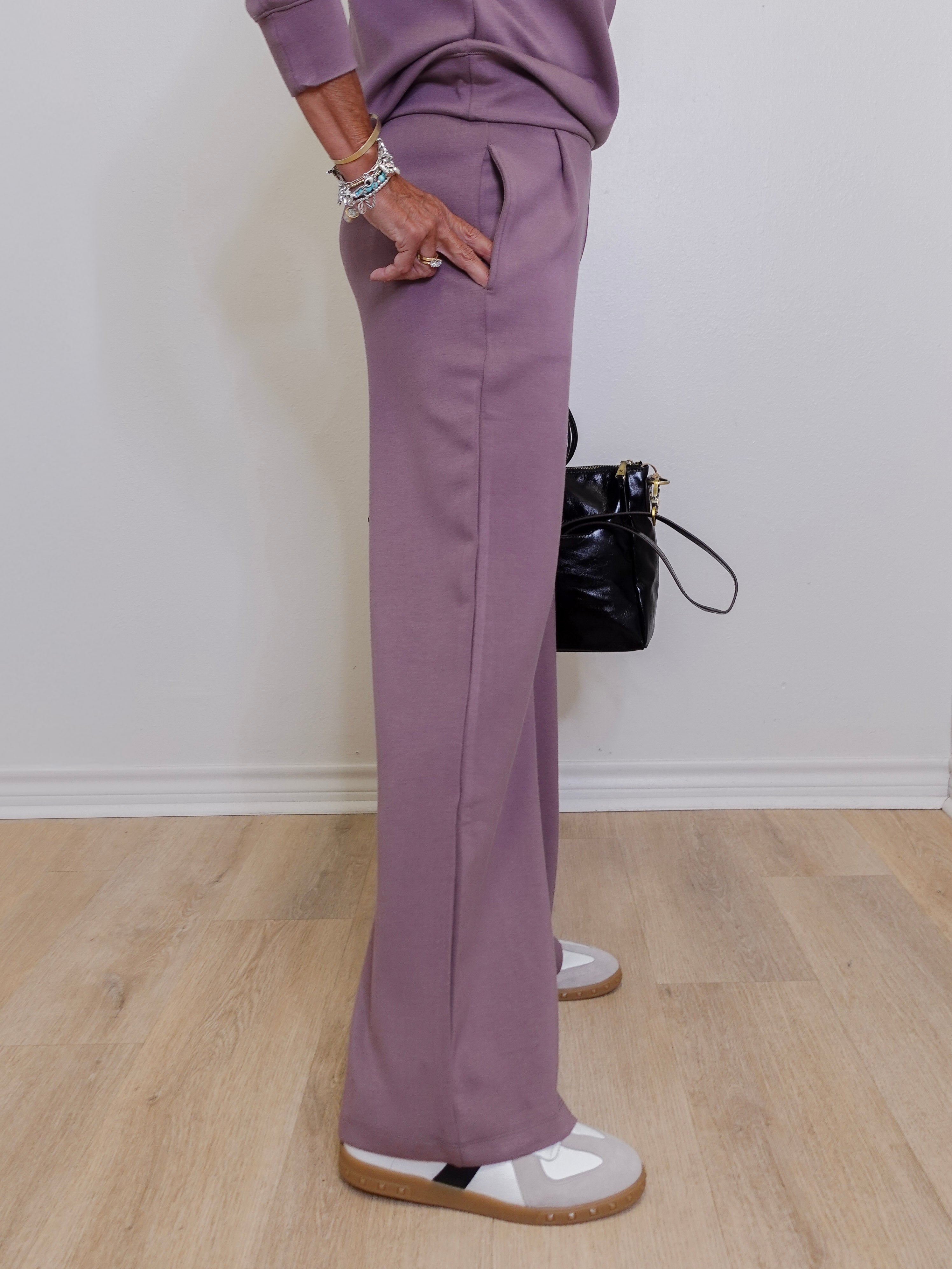 Person wearing a matching purple outfit with wide-leg pants and a black bag on a wooden floor.