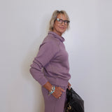 Woman in a purple outfit holding a black handbag against a white wall