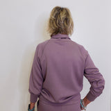Person wearing a purple tracksuit against a white wall