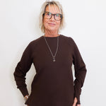 Woman wearing a brown sweater and glasses against a white background