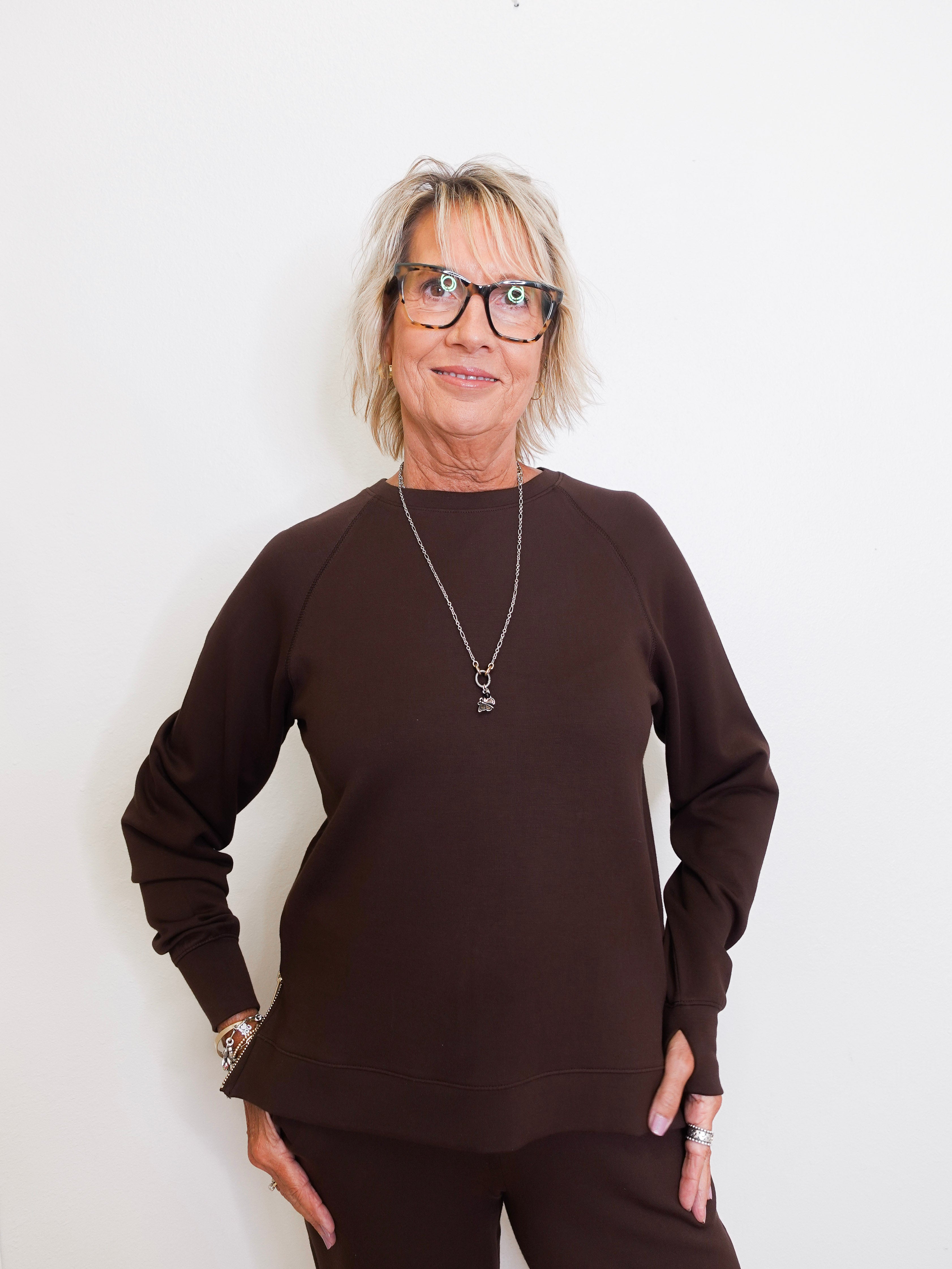 Woman wearing a brown sweater and glasses against a white background