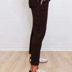 Person wearing black pants and white sneakers with black accents on a light wooden floor.