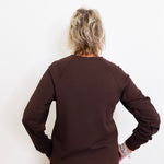 Person wearing a brown long-sleeve top and pants against a white background