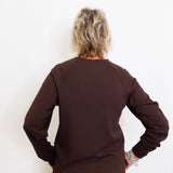 Person wearing a brown long-sleeve top and pants against a white background