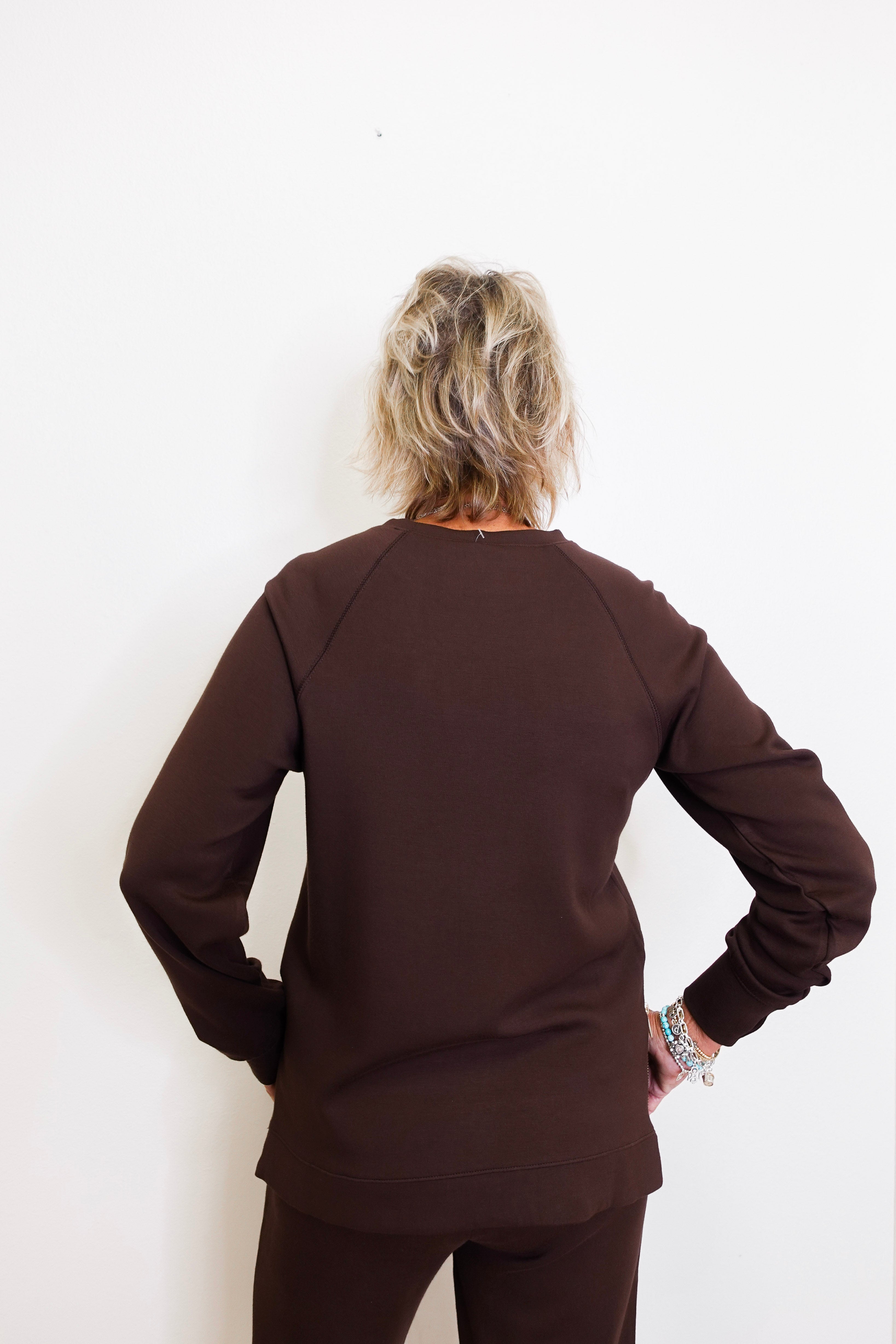 Person wearing a brown long-sleeve top and pants against a white background
