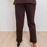 Person wearing brown pants and a matching top on a light wooden floor with a white wall background