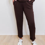 Person wearing brown pants and white sneakers against a white wall.