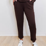 Person wearing brown pants and white sneakers against a white wall.