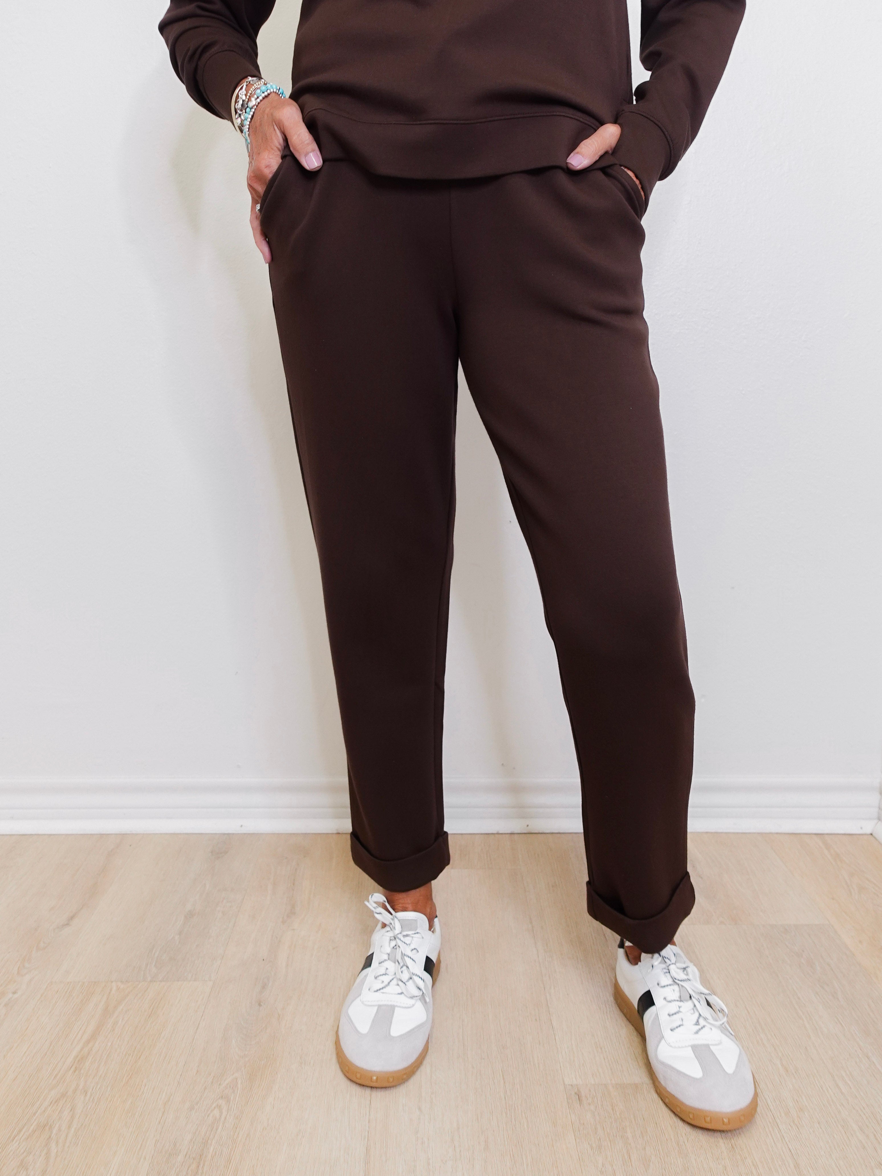Person wearing brown pants and white sneakers against a white wall.
