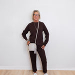 Person wearing a brown outfit with white sneakers against a white wall