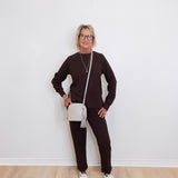 Person wearing a brown outfit with white sneakers against a white wall