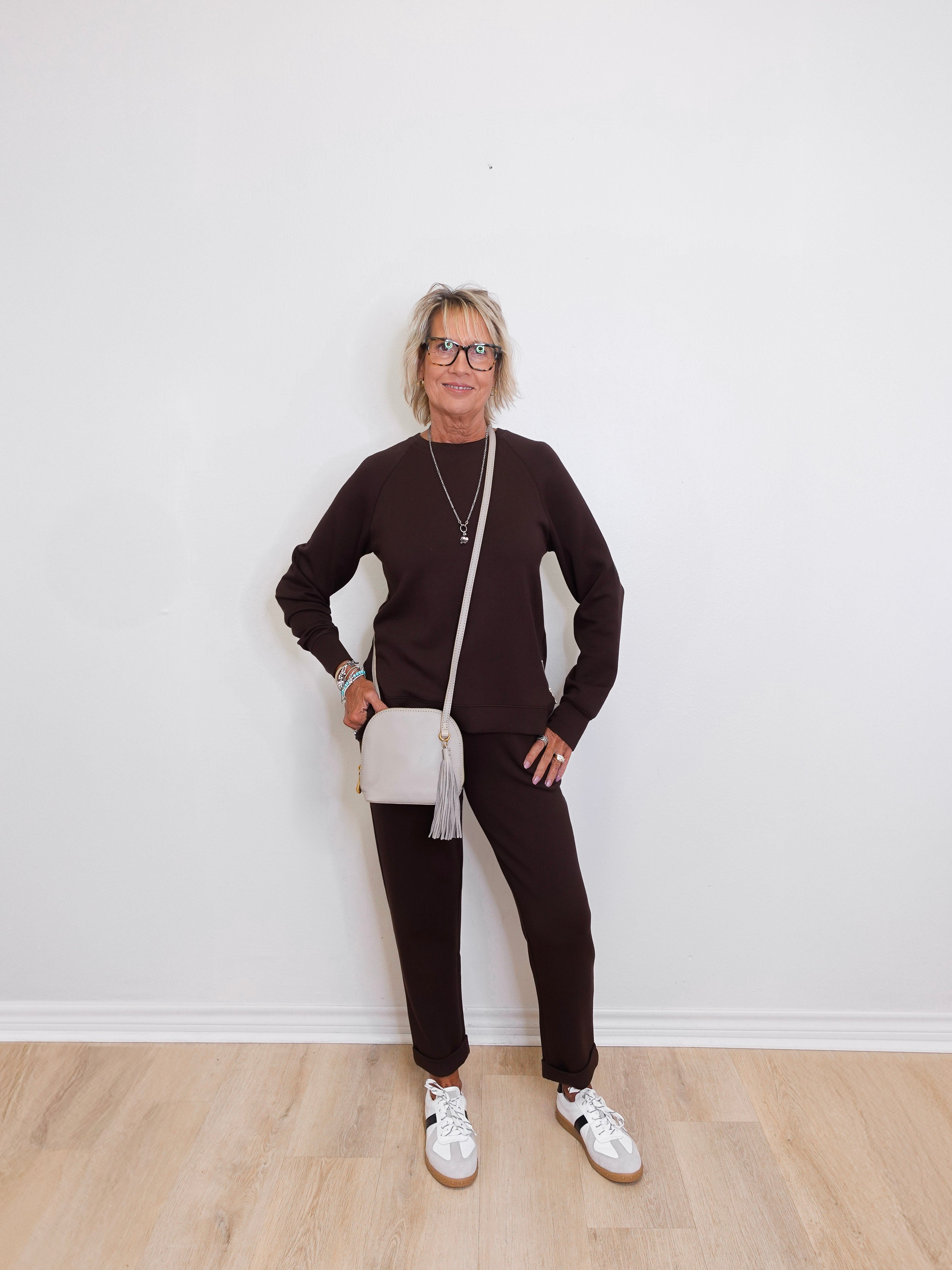 Person wearing a brown outfit with white sneakers against a white wall