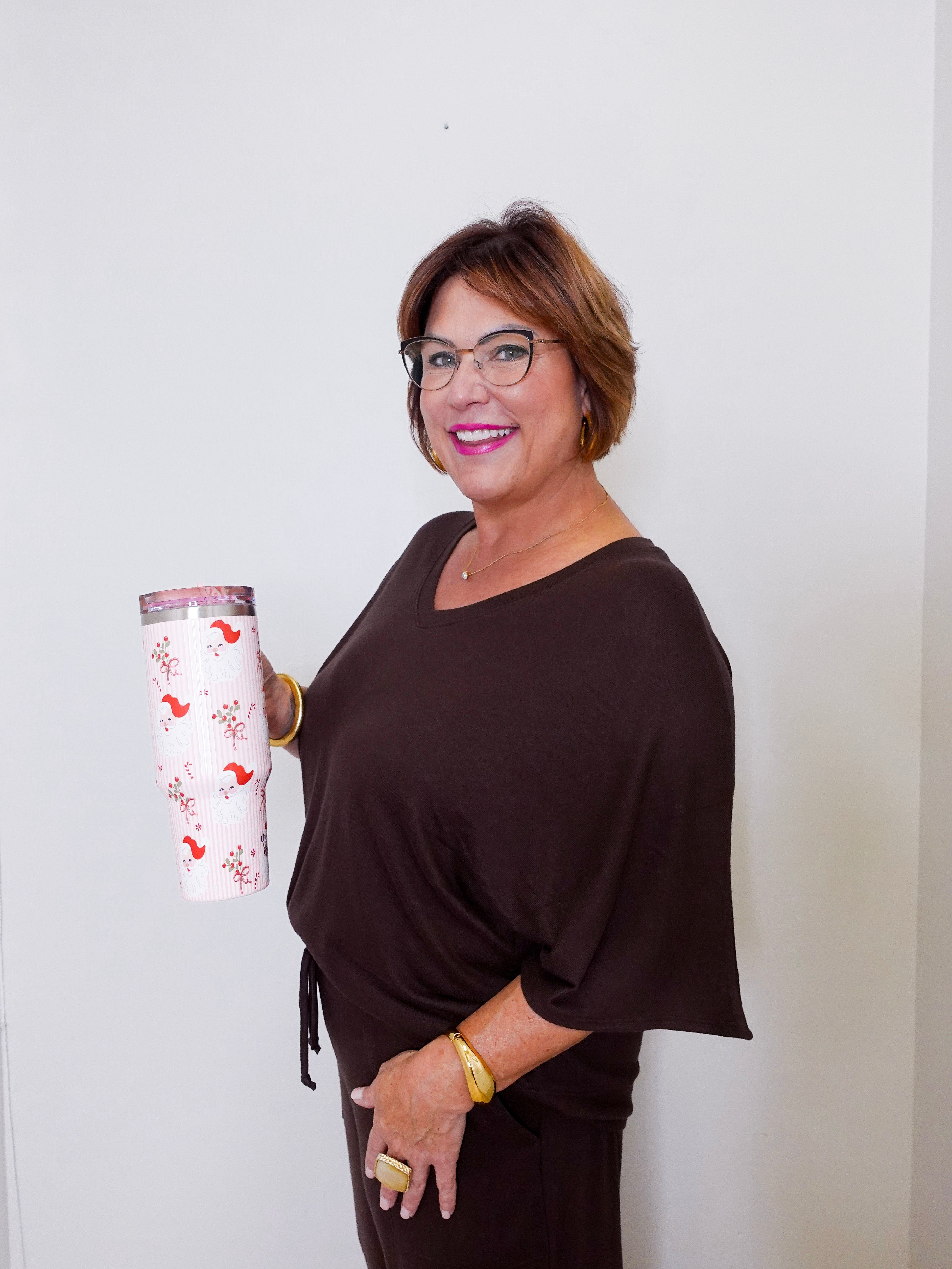 Woman holding a white tumbler with a floral design against a plain background