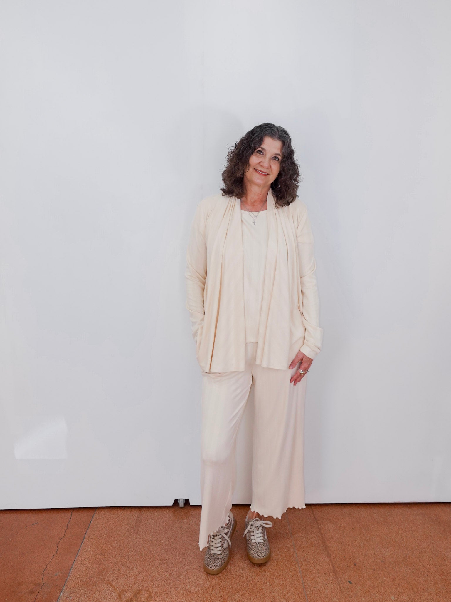 Woman in a beige outfit standing against a white wall
