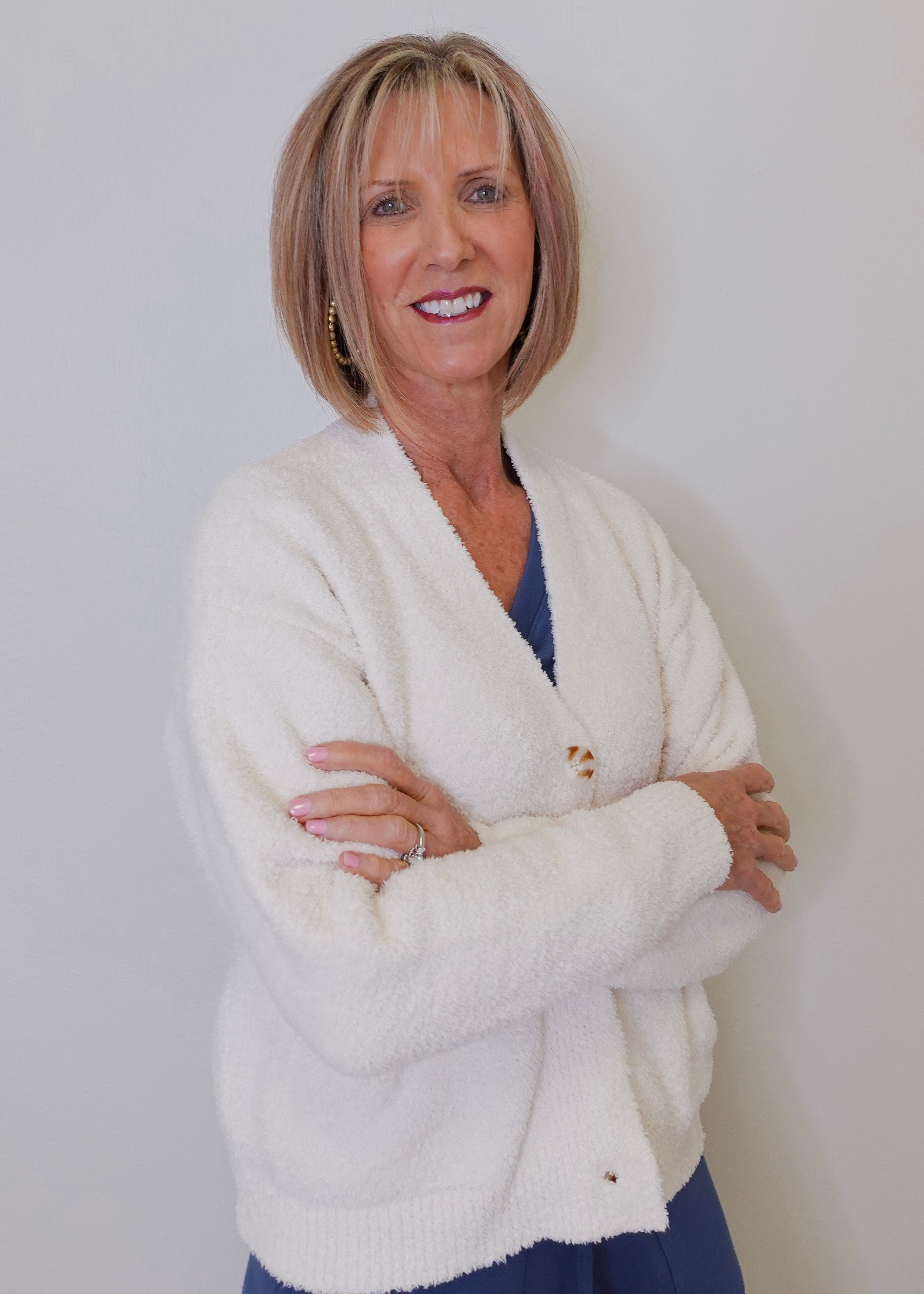 A person wearing a white crop cardigan with long sleeves, displayed in a frontal pose with arms crossed.