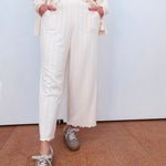 Person wearing a cream outfit with white pants and gray sneakers on a plain background