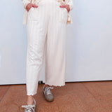 Person wearing a cream outfit with white pants and gray sneakers on a plain background