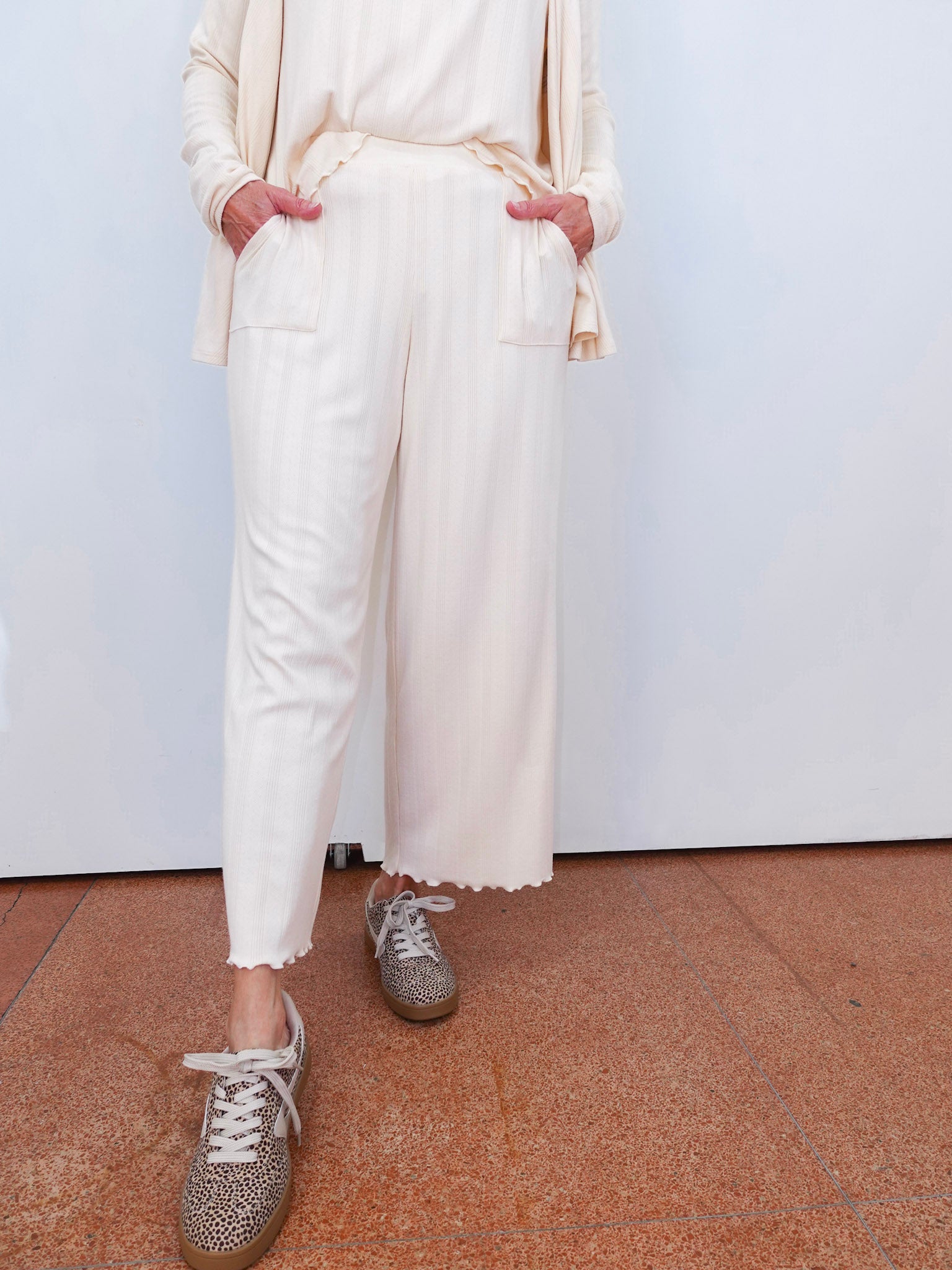 Person wearing a cream outfit with white pants and gray sneakers on a plain background