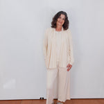 Woman in a beige outfit standing against a white wall