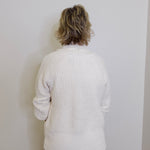 Person wearing a white textured sweater against a plain white background