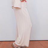 Person wearing a white outfit with wide-leg pants and patterned shoes on a plain background