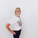 Person wearing a white t-shirt with a colorful graphic and dark jeans on a plain background