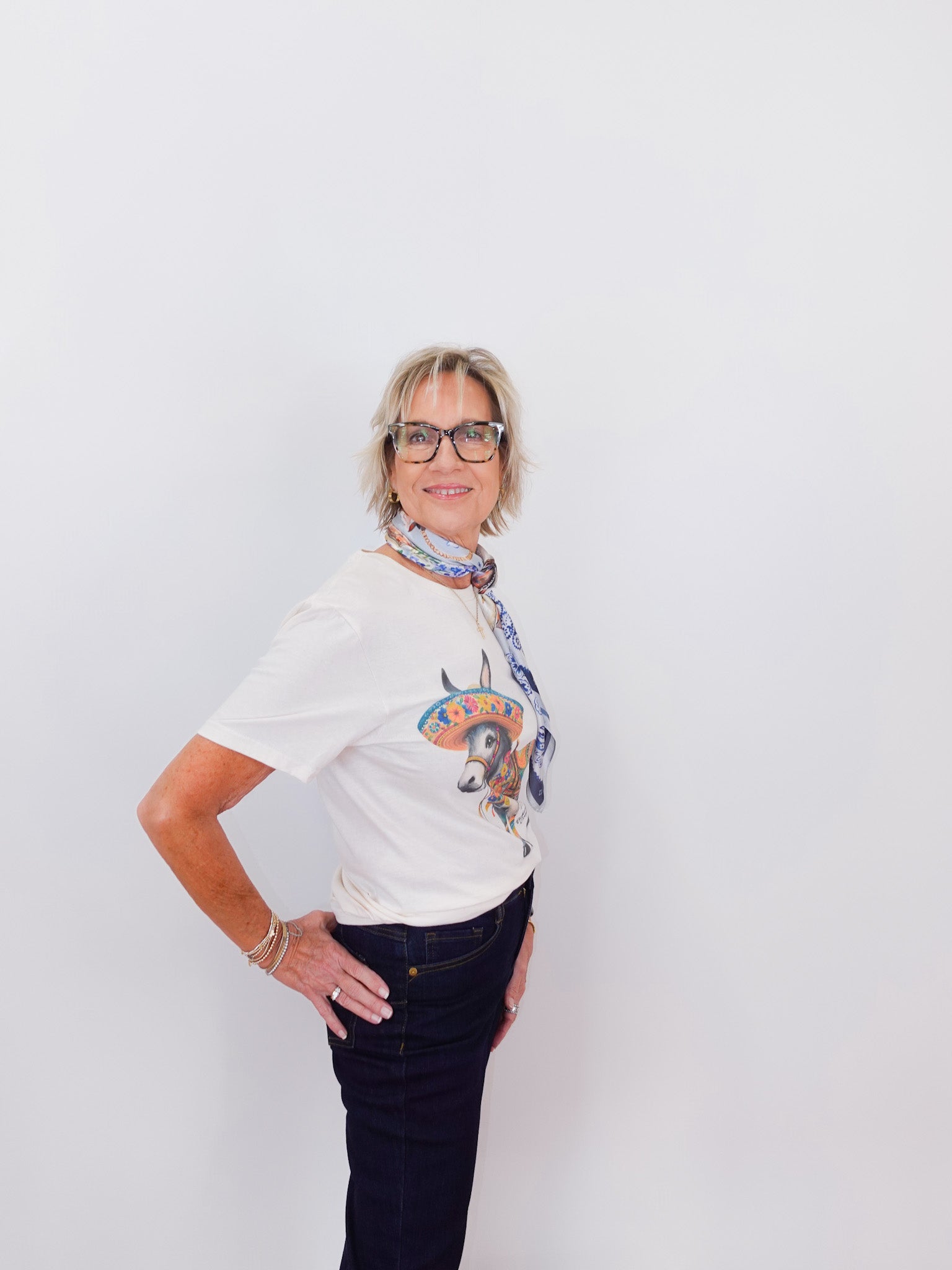 Person wearing a white t-shirt with a colorful graphic and dark jeans on a plain background