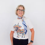 Woman wearing a white t-shirt with a colorful bull graphic and a blue scarf, standing against a white background.