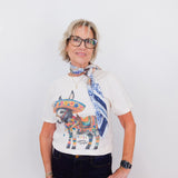 Woman wearing a white t-shirt with a colorful bull graphic and a blue scarf, standing against a white background.