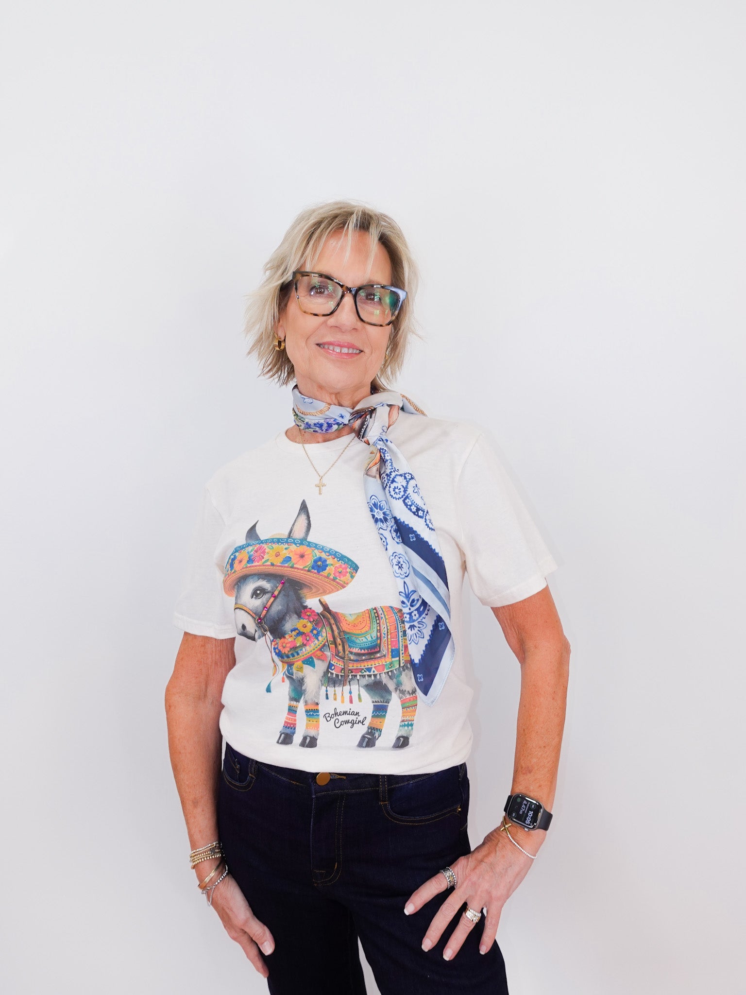 Woman wearing a white t-shirt with a colorful bull graphic and a blue scarf, standing against a white background.