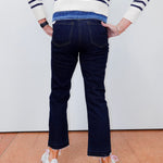Person wearing a striped sweater and dark jeans standing against a white wall.