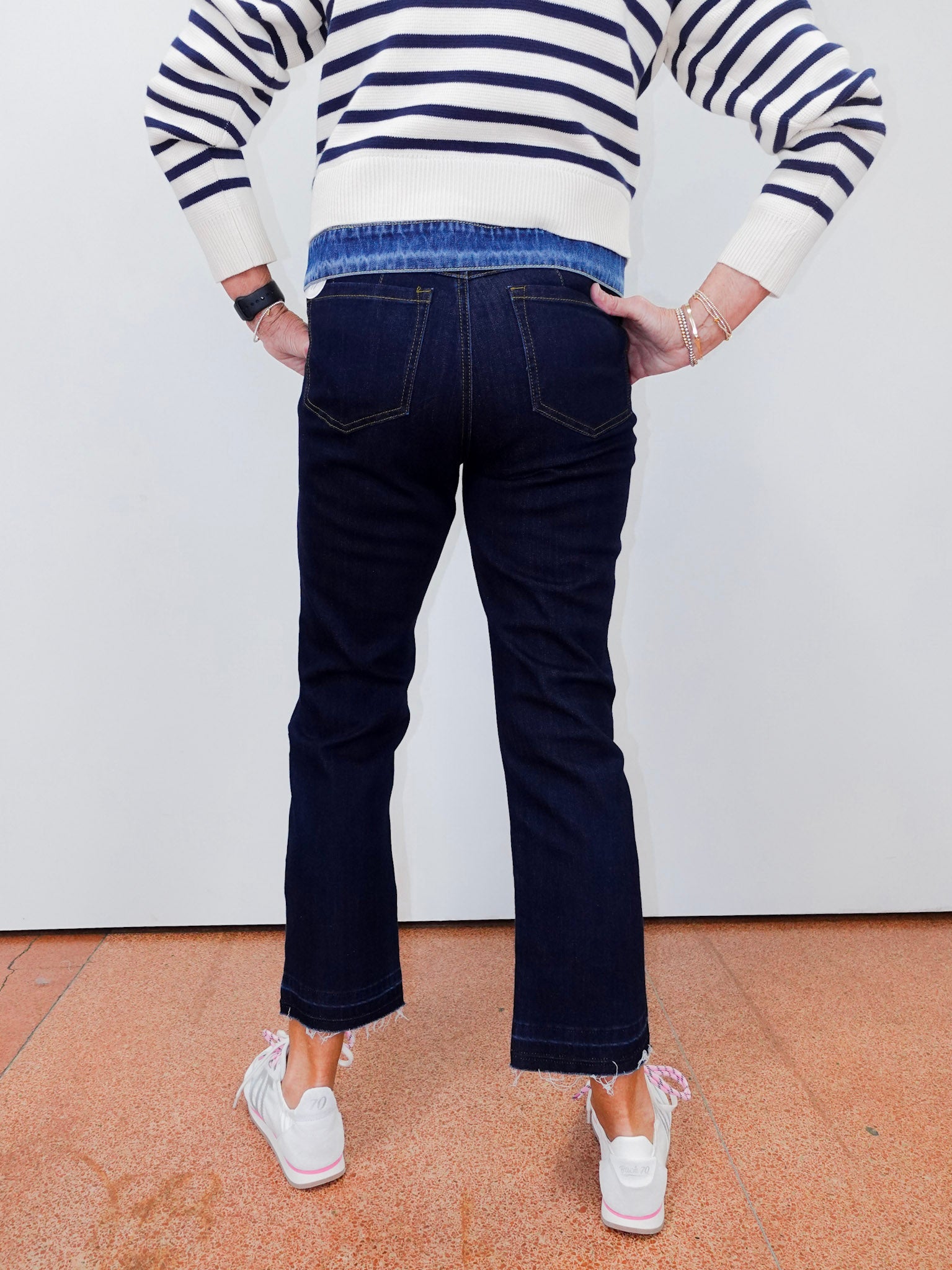 Person wearing a striped sweater and dark jeans standing against a white wall.
