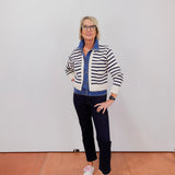 Person wearing a striped sweater and dark pants standing against a white wall.