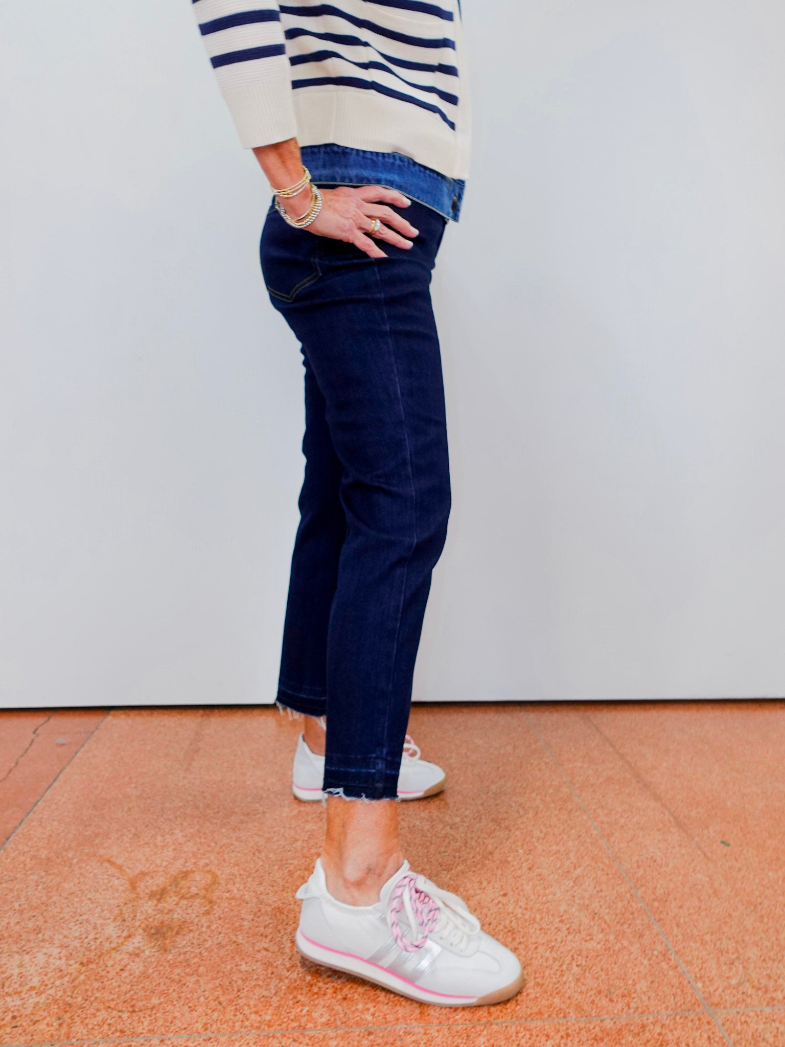 Person wearing a striped sweater, blue jeans, and white sneakers on a plain background