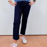 Person wearing a striped sweater, denim jacket, navy pants, and white sneakers on a plain background