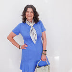 Woman wearing a blue dress with a white scarf and holding a green handbag against a white background