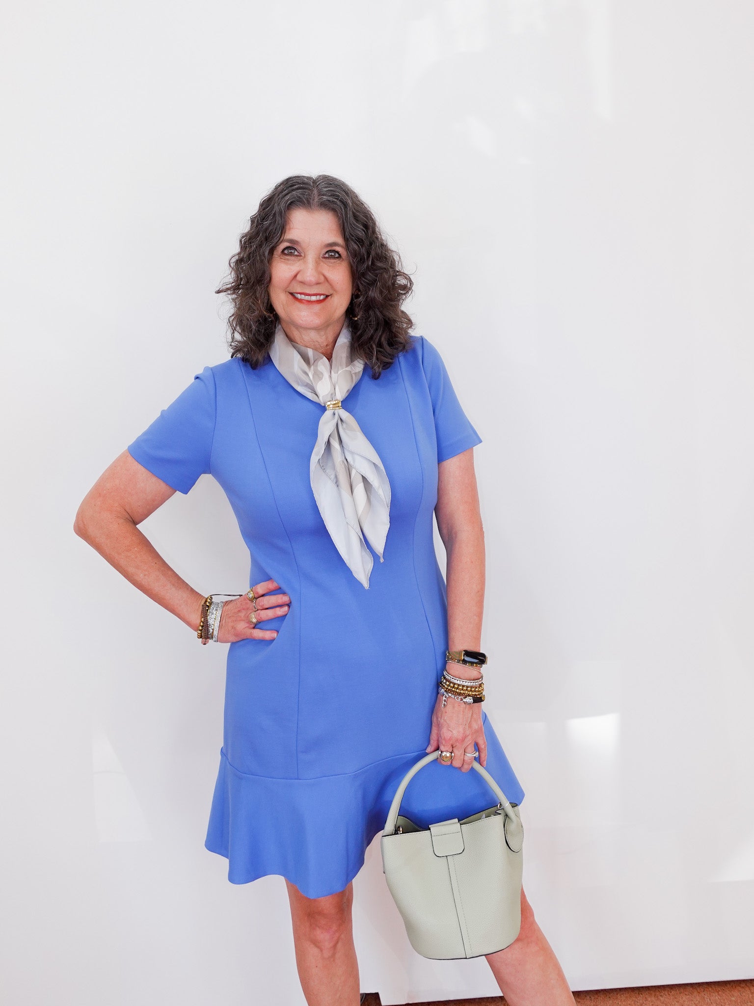 Woman wearing a blue dress with a white scarf and holding a green handbag against a white background