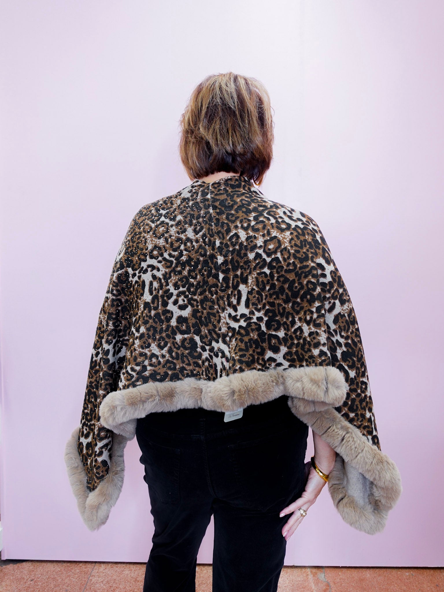 Person wearing a leopard print coat with fur trim on a plain background