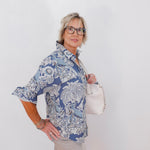 Woman wearing a blue patterned shirt holding a white handbag against a white background