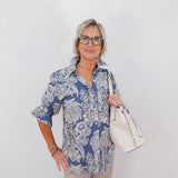 Woman wearing a blue patterned shirt and holding a white handbag against a white background