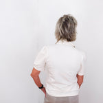 Person wearing a white polo shirt and beige pants against a white background