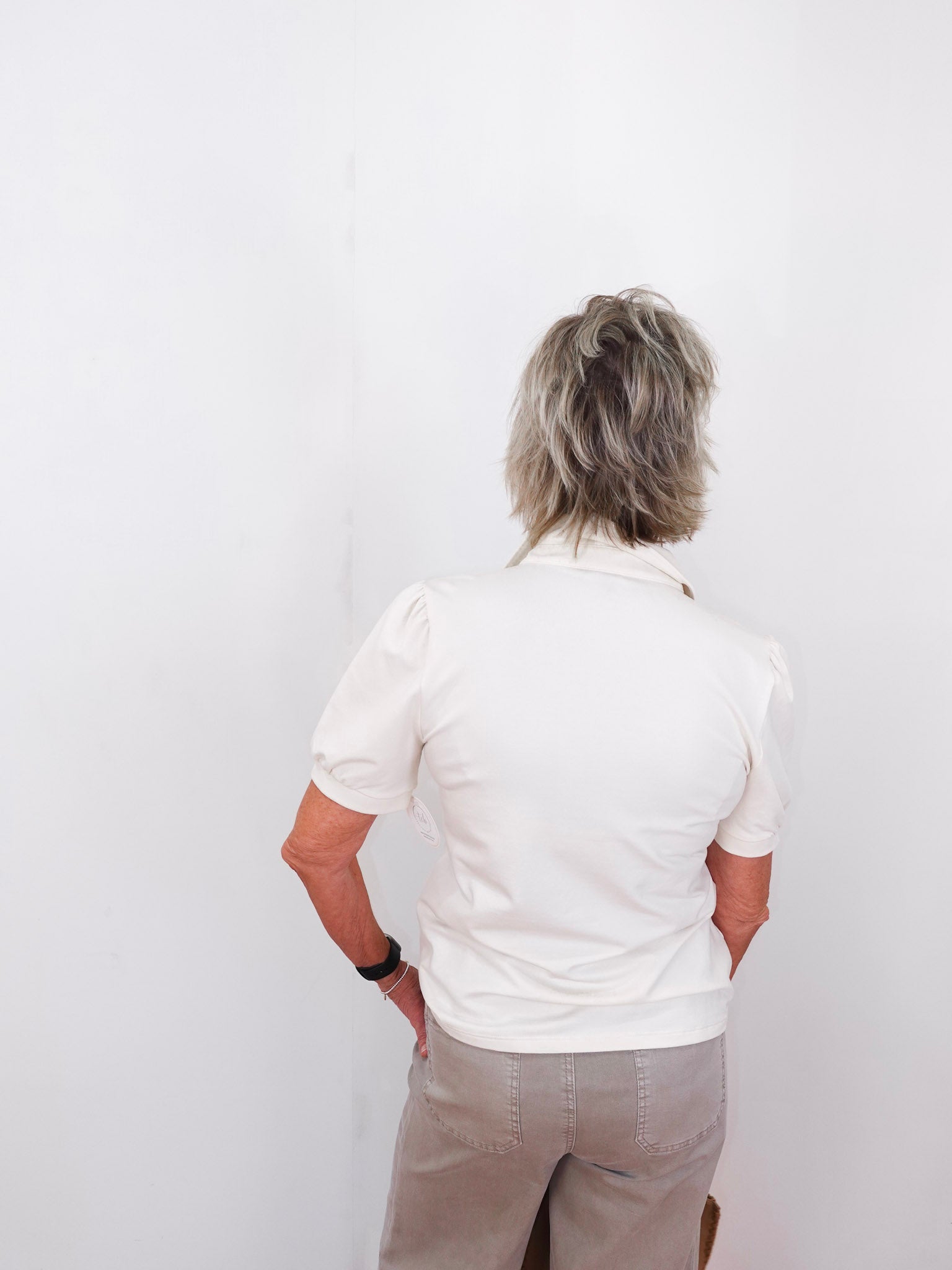 Person wearing a white polo shirt and beige pants against a white background