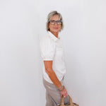 Woman holding a beige handbag against a white wall