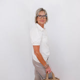 Woman holding a beige handbag against a white wall