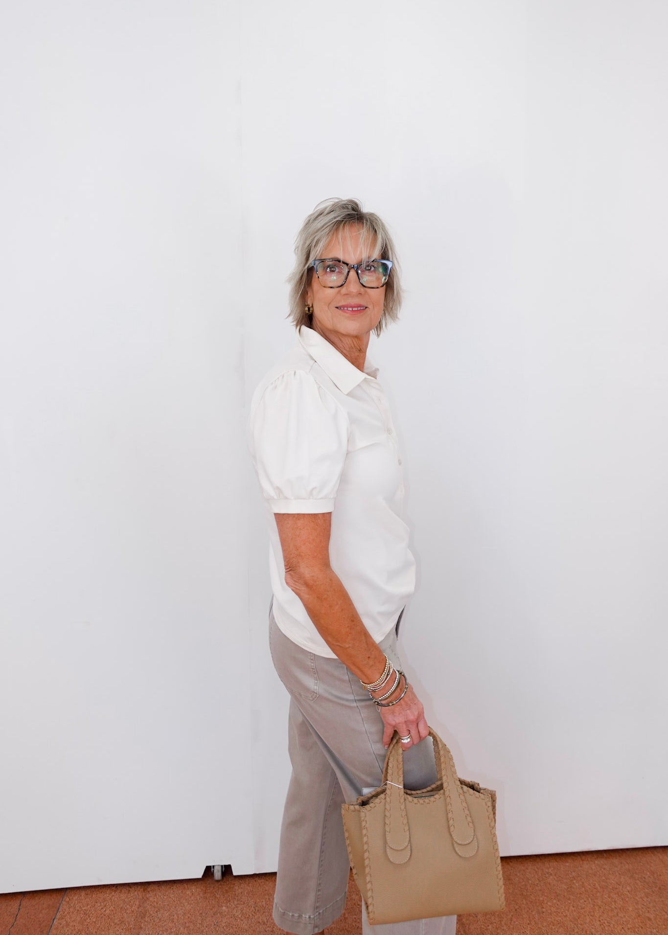 Woman holding a beige handbag against a white wall