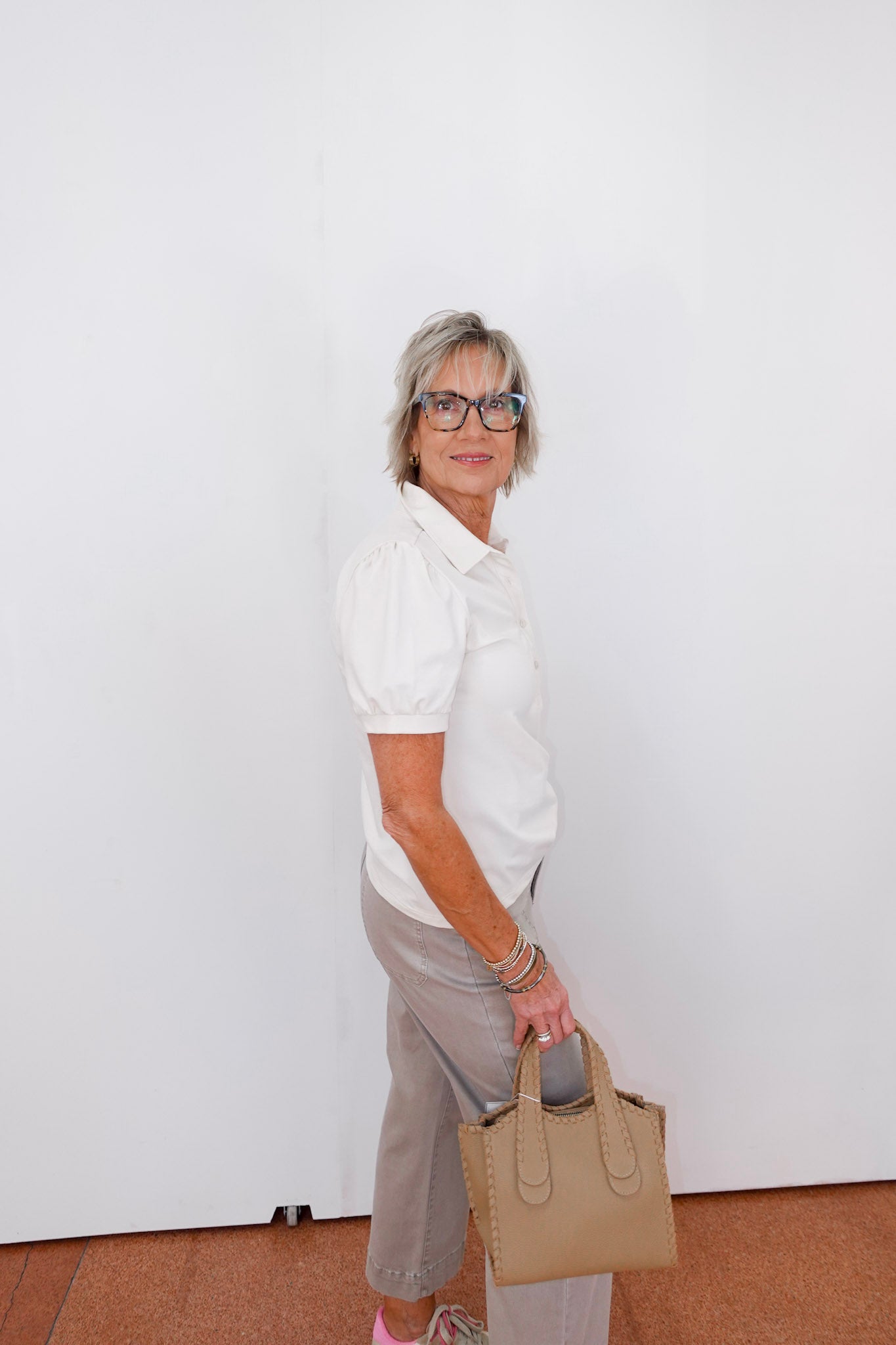 Woman holding a beige handbag against a white wall