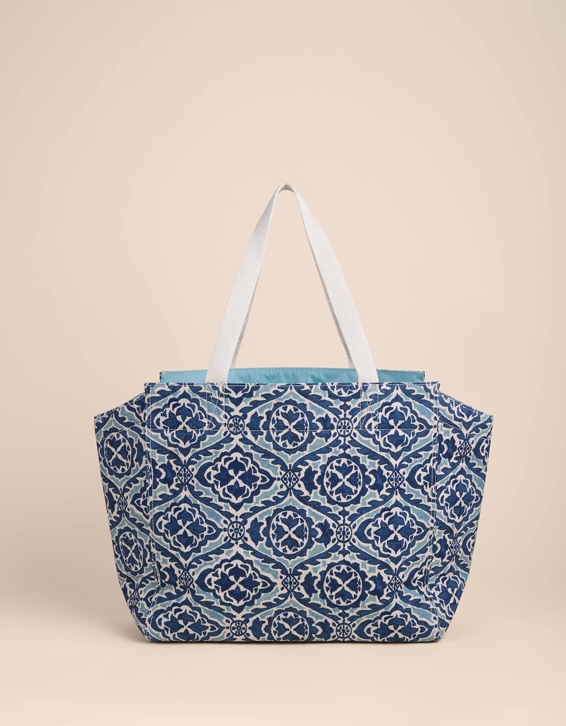 Blue patterned tote bag with white straps on a beige background